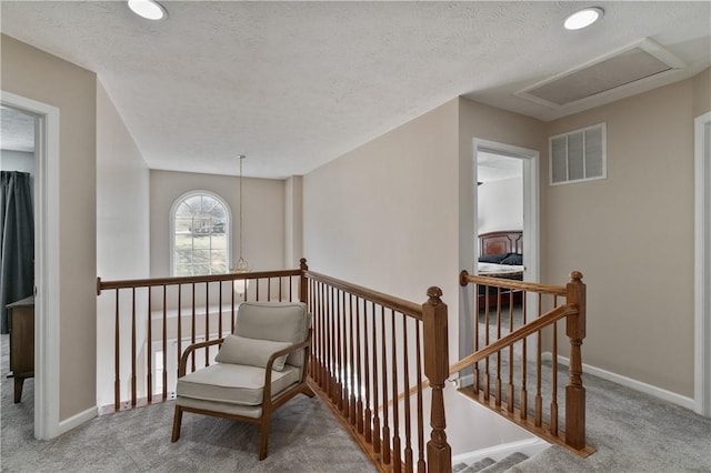 corridor featuring visible vents, an upstairs landing, a textured ceiling, carpet floors, and baseboards