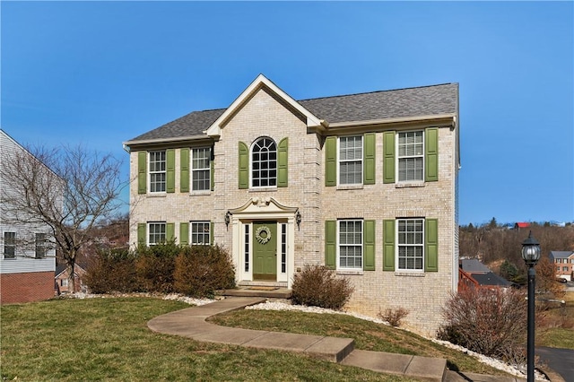 colonial house featuring a front lawn and brick siding