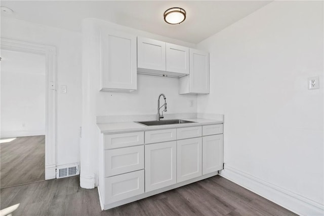 kitchen with light countertops, white cabinets, dark wood-style floors, and a sink