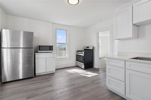 kitchen featuring white cabinets, appliances with stainless steel finishes, light wood-style floors, and light stone countertops