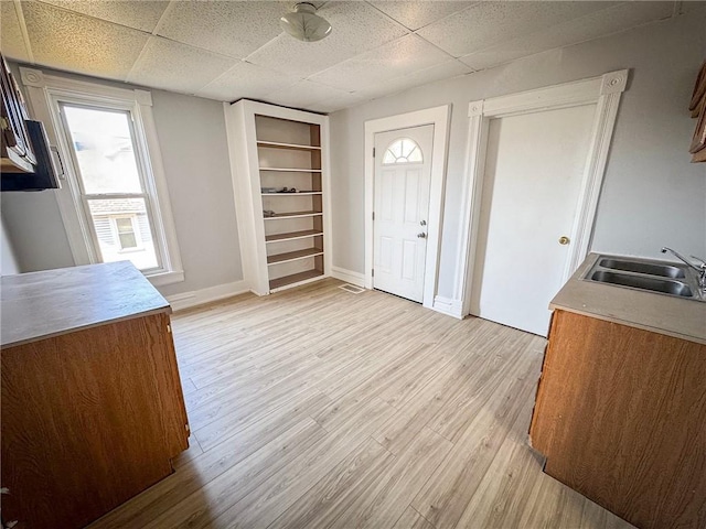 foyer with a drop ceiling, baseboards, and light wood finished floors