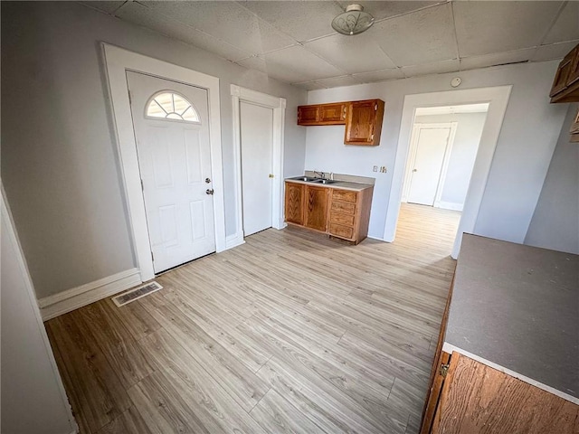 kitchen with visible vents, light wood finished floors, a sink, brown cabinetry, and light countertops