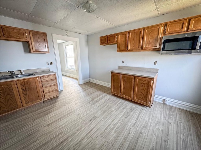 kitchen featuring light wood-type flooring, brown cabinets, a sink, stainless steel microwave, and a drop ceiling