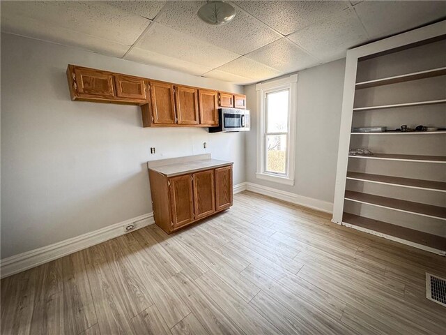 kitchen featuring stainless steel microwave, brown cabinets, baseboards, and light wood finished floors