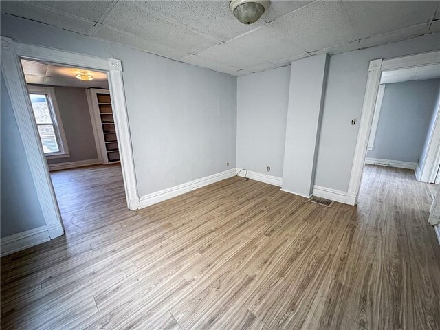 unfurnished room with baseboards, a paneled ceiling, and wood finished floors