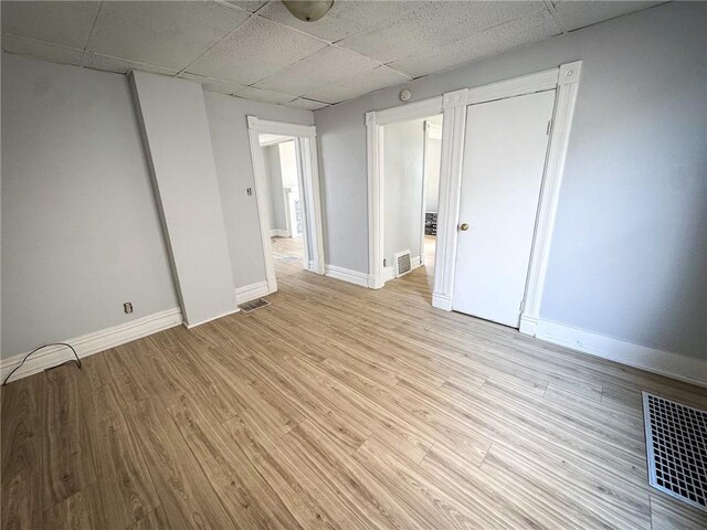 empty room featuring visible vents, light wood-style flooring, and a drop ceiling