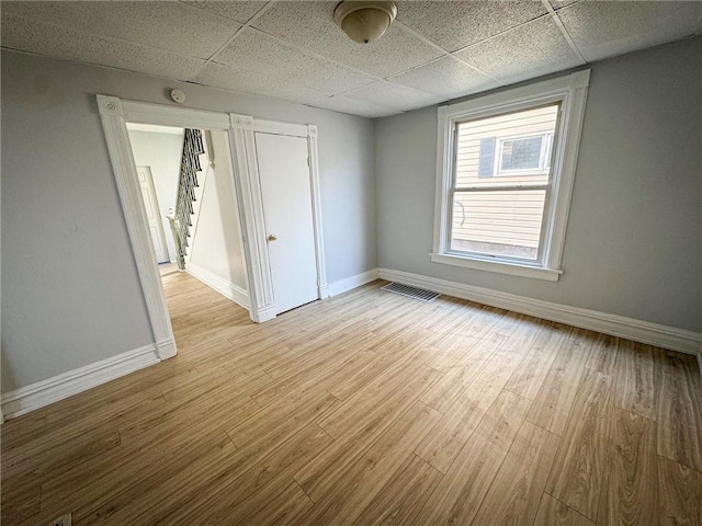 unfurnished room with light wood finished floors, stairway, baseboards, and a drop ceiling