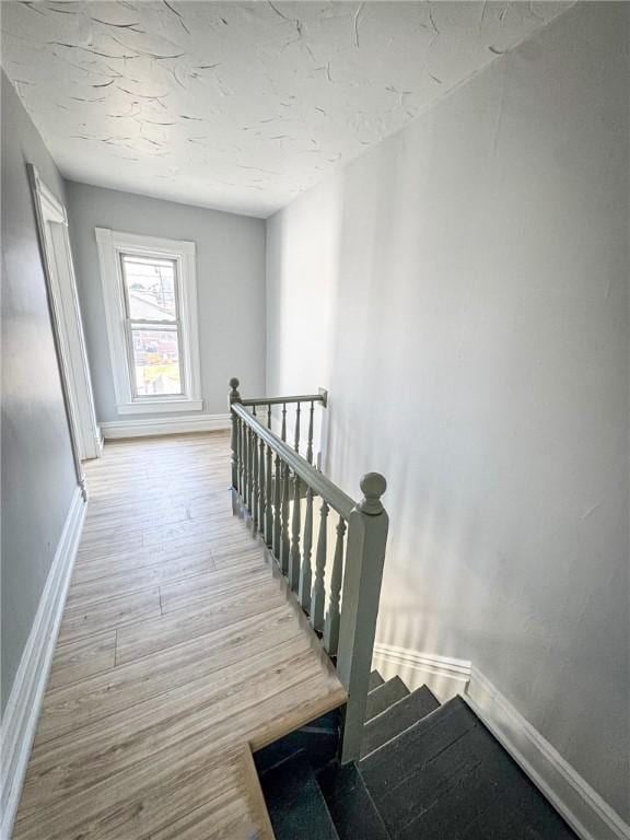 stairway featuring a textured ceiling, baseboards, and wood finished floors