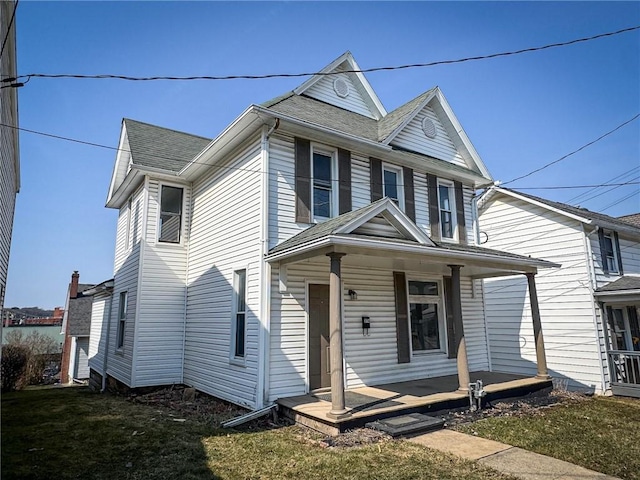 view of front facade with roof with shingles, covered porch, and a front yard