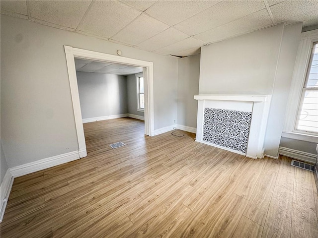 unfurnished living room featuring a drop ceiling, baseboards, visible vents, and wood finished floors