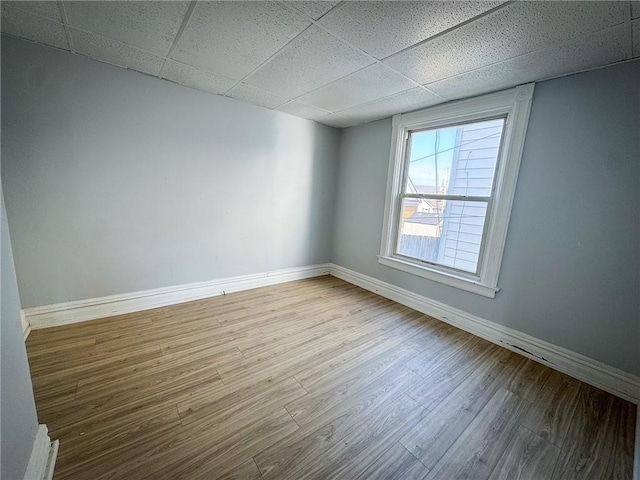 spare room featuring a drop ceiling, baseboards, and wood finished floors