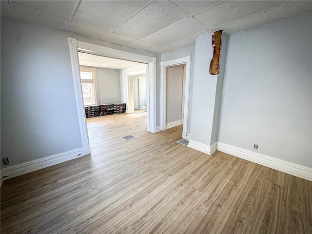 empty room with visible vents, wood finished floors, baseboards, and a drop ceiling