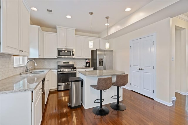 kitchen with a sink, appliances with stainless steel finishes, dark wood-style floors, and white cabinetry