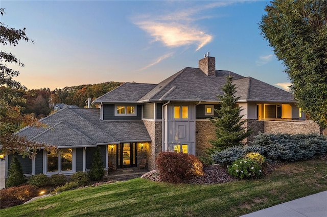 view of front of home featuring stone siding, a lawn, and a chimney