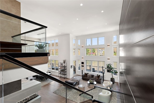 living area with a wealth of natural light, recessed lighting, wood finished floors, and a towering ceiling