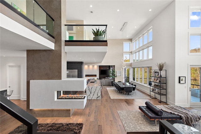 living area with wood finished floors, baseboards, recessed lighting, a multi sided fireplace, and a towering ceiling