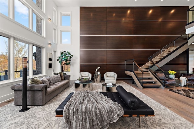 living room with a towering ceiling, baseboards, wood finished floors, and stairs