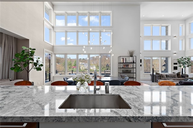 kitchen featuring a high ceiling, light stone counters, open floor plan, and a sink