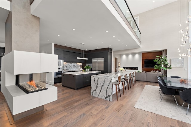 kitchen with modern cabinets, wood finished floors, appliances with stainless steel finishes, a multi sided fireplace, and a large island with sink