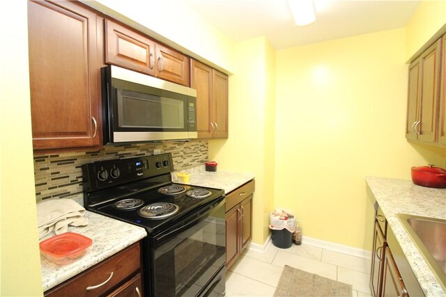 kitchen with electric range, a sink, stainless steel microwave, decorative backsplash, and baseboards