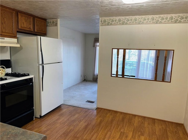 kitchen with visible vents, under cabinet range hood, range with gas stovetop, light wood-style flooring, and brown cabinets