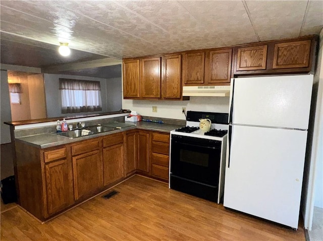 kitchen with range with gas stovetop, wood finished floors, freestanding refrigerator, under cabinet range hood, and brown cabinets