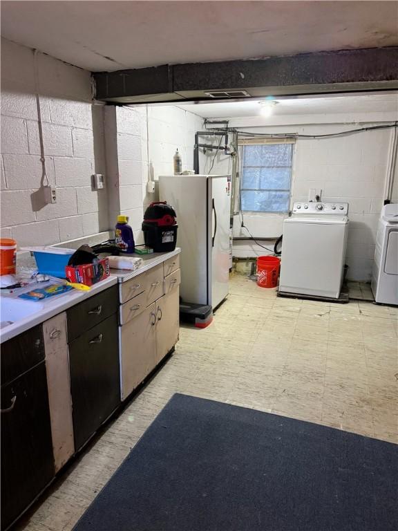 below grade area with concrete block wall, light floors, freestanding refrigerator, and washing machine and clothes dryer