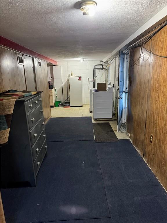 finished basement featuring refrigerator, independent washer and dryer, wood walls, and a textured ceiling