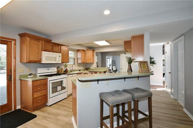 kitchen with white appliances, a breakfast bar area, light countertops, and light wood-style floors