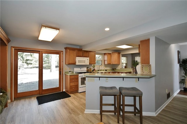 kitchen with a breakfast bar, white appliances, light wood-style floors, and a sink