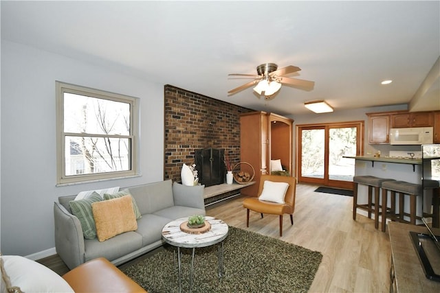 living area with a ceiling fan, recessed lighting, light wood finished floors, baseboards, and a brick fireplace