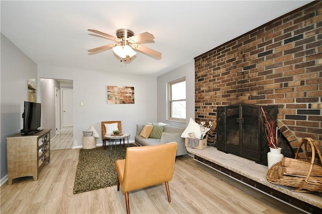 living room with light wood-type flooring, baseboards, a ceiling fan, and a fireplace