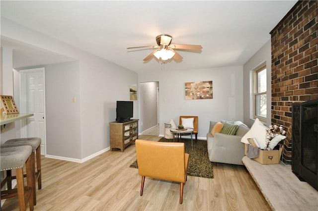 living room featuring ceiling fan, a fireplace, light wood-type flooring, and baseboards