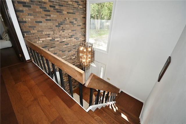 stairs featuring wood finished floors, baseboards, brick wall, a towering ceiling, and a chandelier