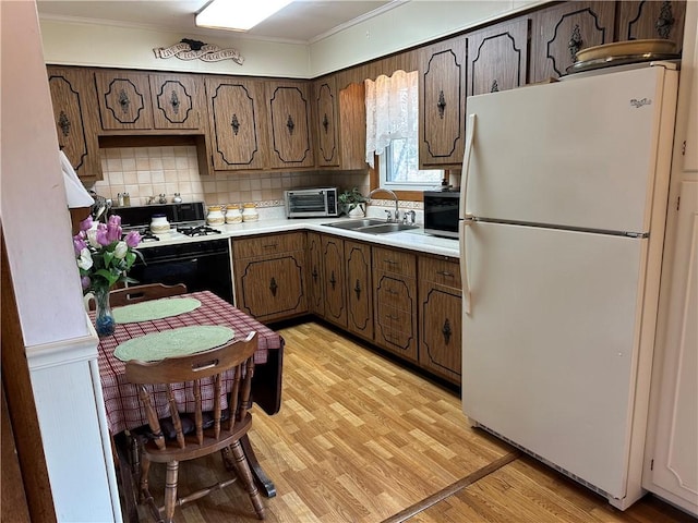 kitchen featuring black gas range, a sink, freestanding refrigerator, wainscoting, and light wood finished floors