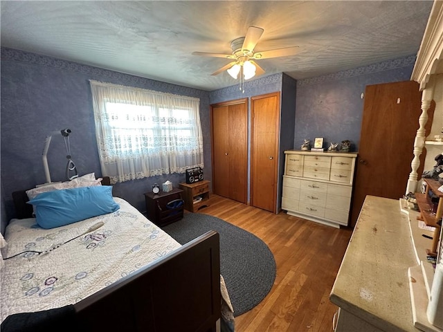 bedroom with wallpapered walls, wood finished floors, two closets, and ceiling fan