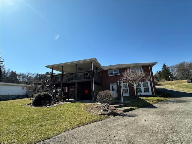 view of front of property with a ceiling fan, a front yard, a wooden deck, brick siding, and stairs