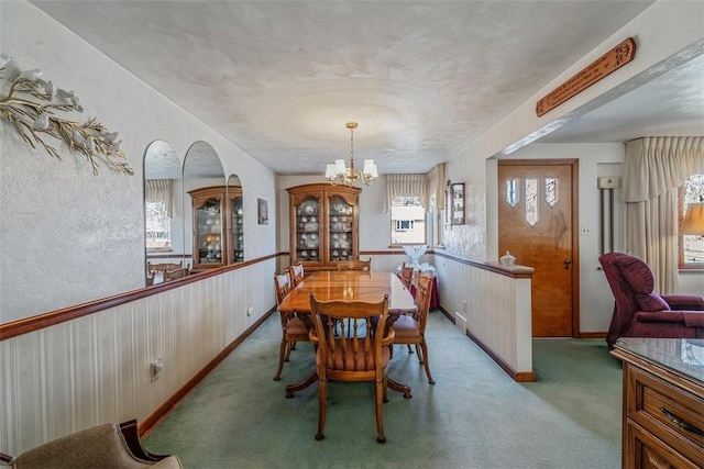 carpeted dining area with an inviting chandelier and wainscoting