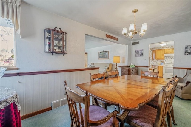 carpeted dining room with wainscoting, visible vents, and a chandelier