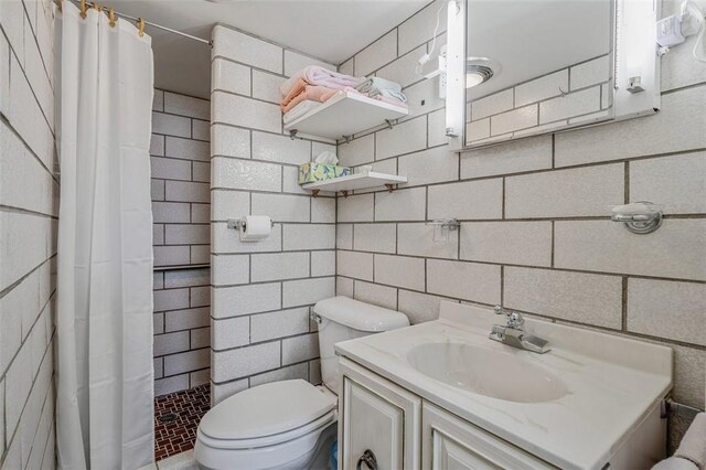 bathroom with tiled shower, vanity, toilet, and tile walls