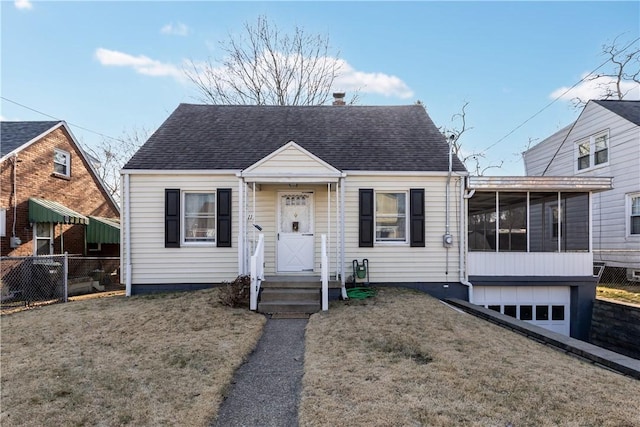 view of front of home with fence, a shingled roof, a front yard, and a sunroom