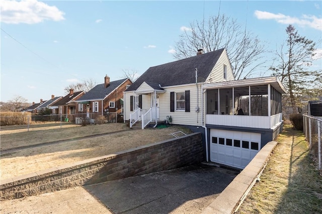 view of front of home with a garage, fence, driveway, and a sunroom