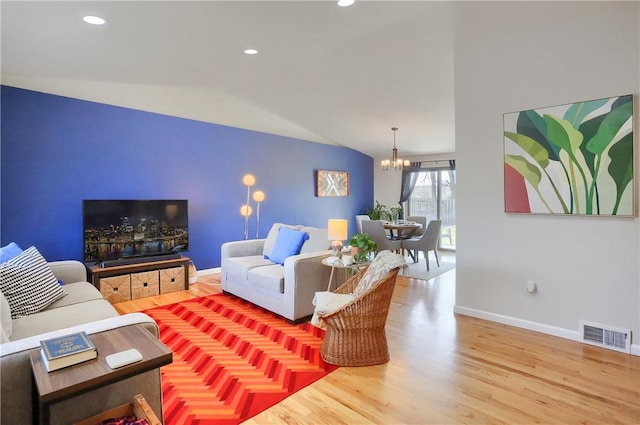 living area featuring wood finished floors, visible vents, baseboards, vaulted ceiling, and a notable chandelier