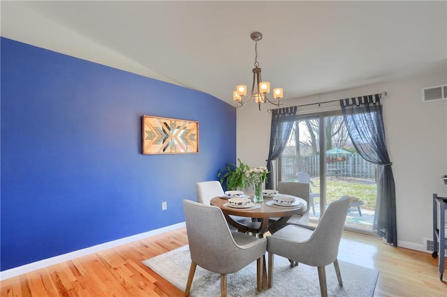 dining area featuring visible vents, baseboards, a chandelier, vaulted ceiling, and wood finished floors