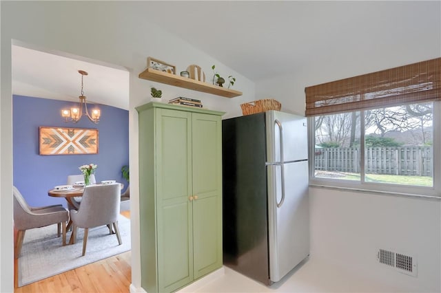 kitchen featuring visible vents, green cabinetry, lofted ceiling, an inviting chandelier, and freestanding refrigerator