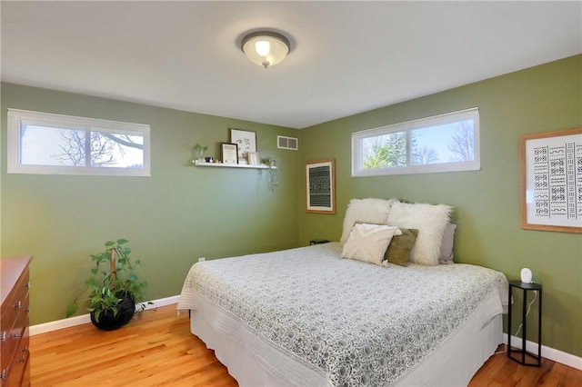 bedroom featuring light wood finished floors, visible vents, multiple windows, and baseboards