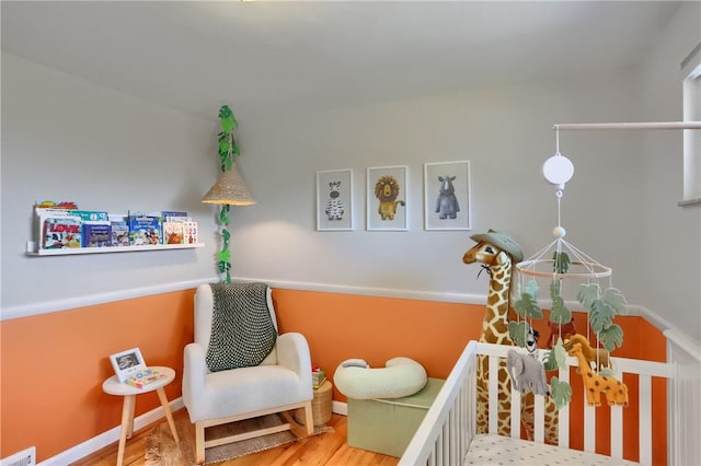 bedroom featuring visible vents, baseboards, a nursery area, and wood finished floors