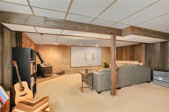 living room featuring a drop ceiling, brick wall, a wood stove, and wood walls