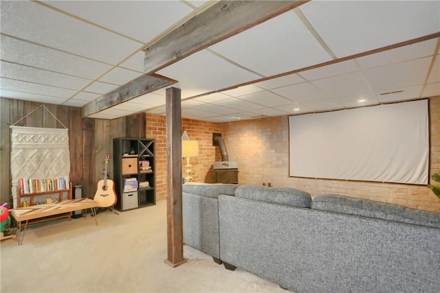 home theater room featuring a wood stove, brick wall, wooden walls, and a drop ceiling