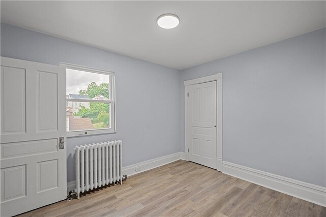 empty room featuring radiator, light wood-type flooring, and baseboards